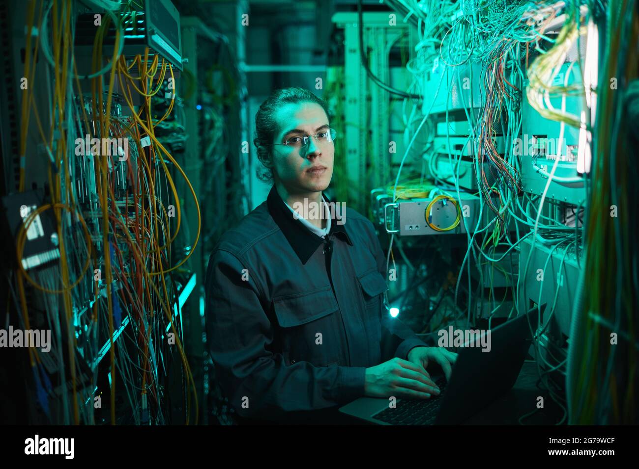 Porträt eines jungen Netzwerktechnikers, der die Kamera im Serverraum betrachtet, während er im Rechenzentrum einen Supercomputer aufsetzt Stockfoto