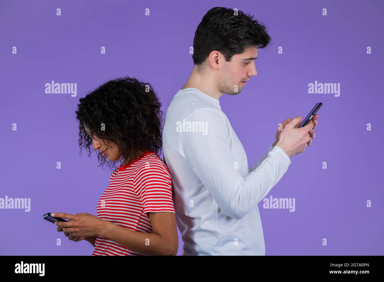 Interrassisches Paar steht mit dem Rücken zueinander und druckt Nachrichten oder surft von Mobiltelefonen aus im Internet. Technologie, Distanzierung, Smartphone Stockfoto