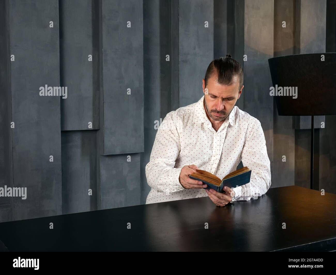 Der Mann im dunklen, modernen Zimmer liest ein altes Buch. Stockfoto