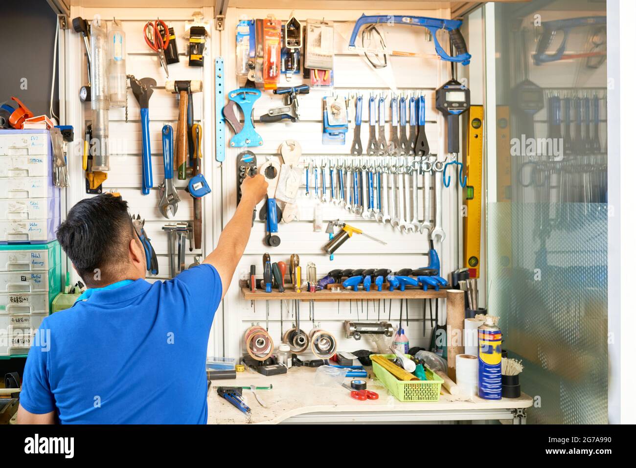 Mechaniker nimmt Werkzeug von der Wand hinter seiner Werkbank, Blick von  hinten Stockfotografie - Alamy