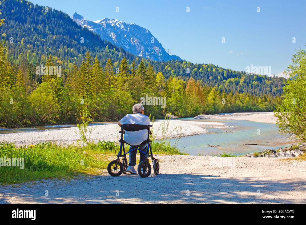 Die Alte sitzt in einem Rollator am Ufer der Isar bei Wallgau und genießt die wunderschöne Landschaft Stockfoto