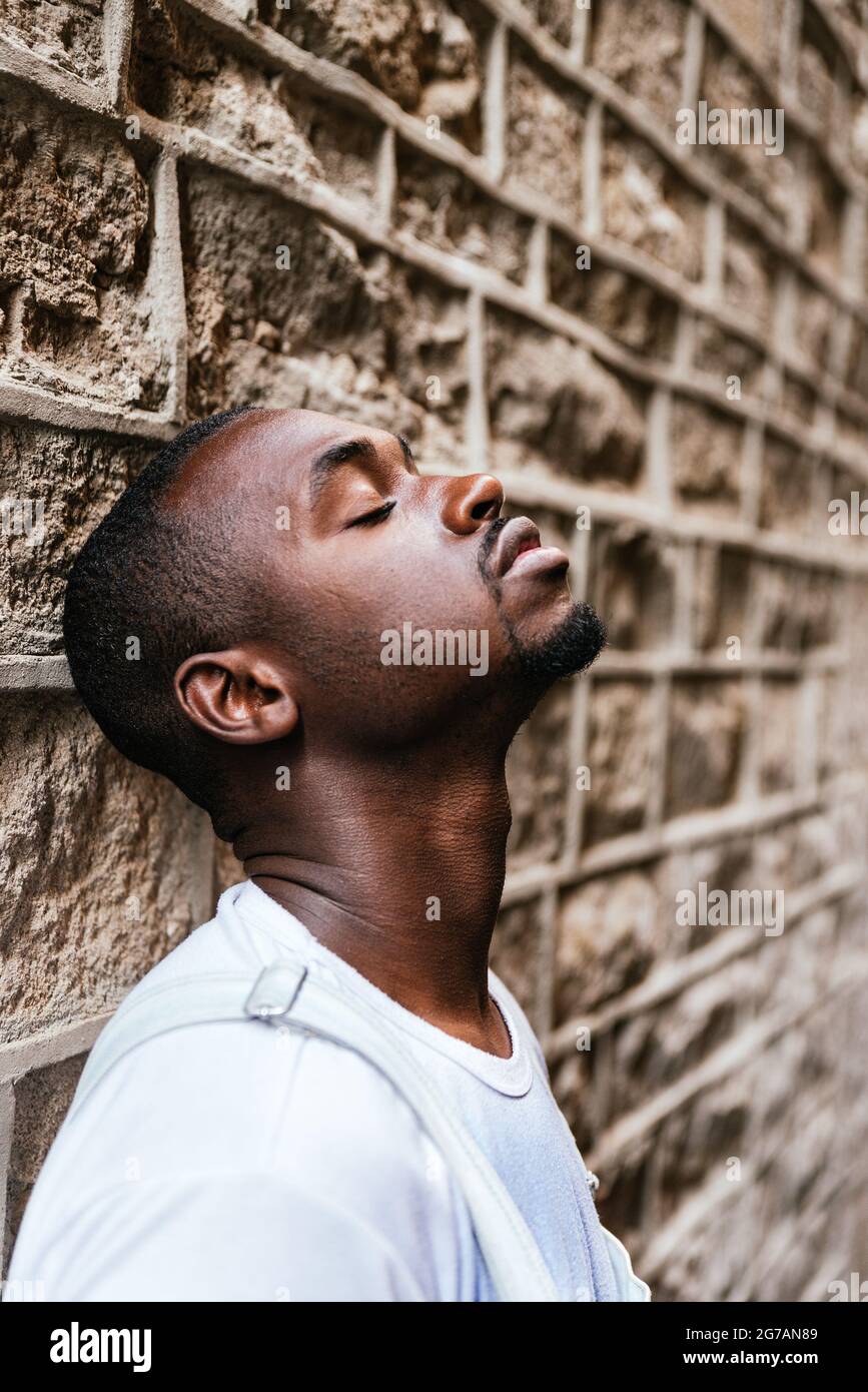 Afro attraktiver Mann, der sich mit geschlossenen Augen an einer Wand lehnt. Konzept der Reflexion, Meditation, eine Pause machen Stockfoto