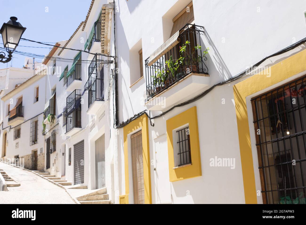 Typische weiße Gipswände mit orangefarbenen Fenstern und Türeinfassungen und schwarzen schmiedeeisernen Balkonen in der Straßenszene Altea, Alicante, Spanien Stockfoto