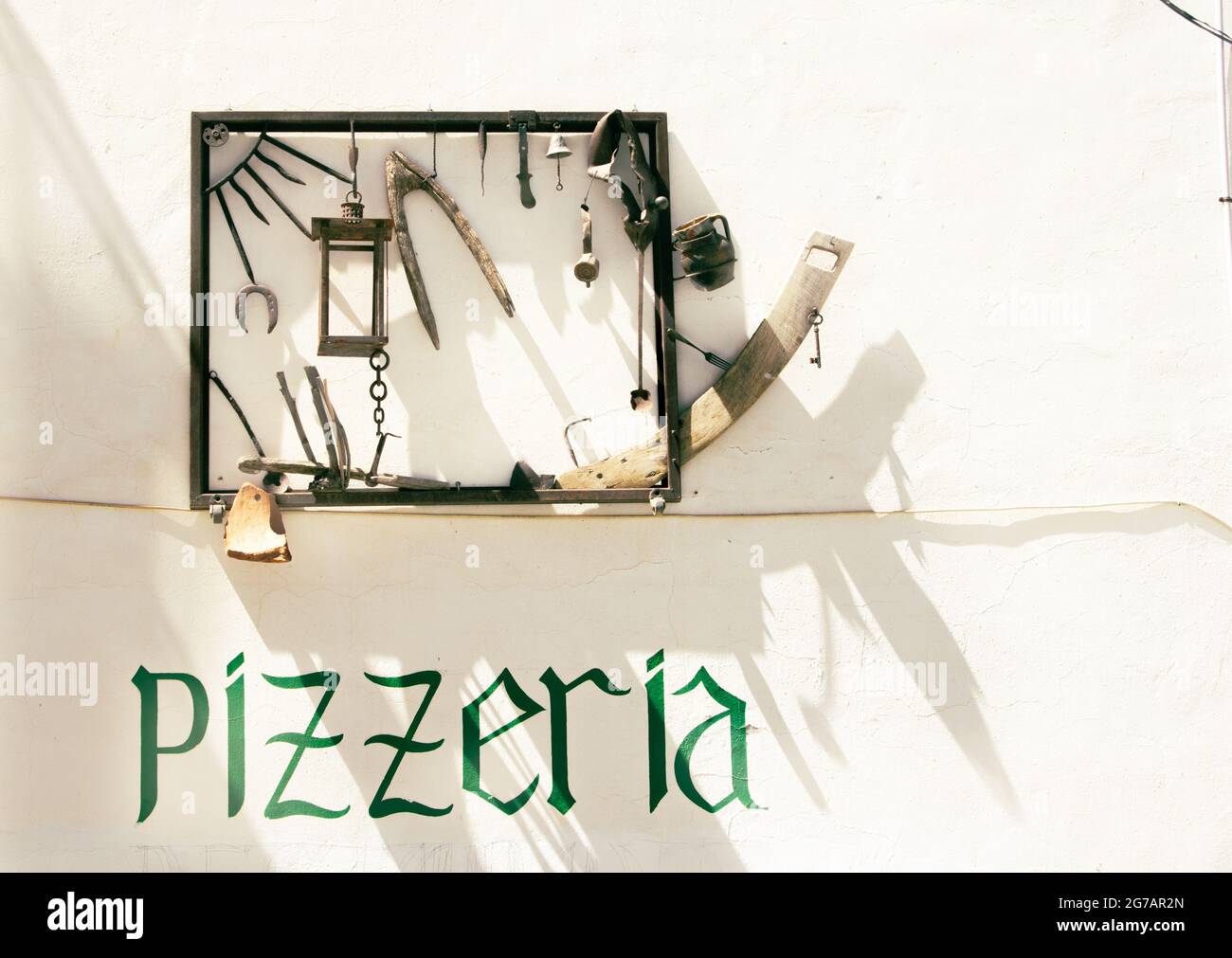 Altea Spanien - August 24 2016; Straßenszene in Altea Pizzeria Schild und skurrile gerahmte Sammlung von Bit und Stücke werfen Schatten auf Außenwand Alic Stockfoto