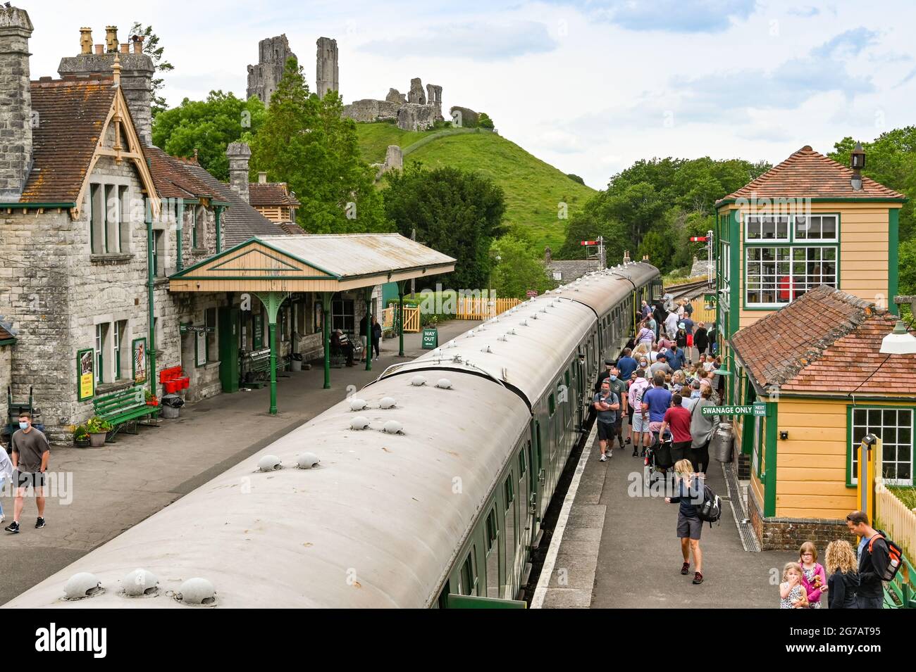 Corfe Castle, Dorset, England - 2021. Juni: Menschen steigen am Bahnhof von Corfe Castle in einen alten Dampfzug. Das Schloss ist im Hintergrund. Stockfoto