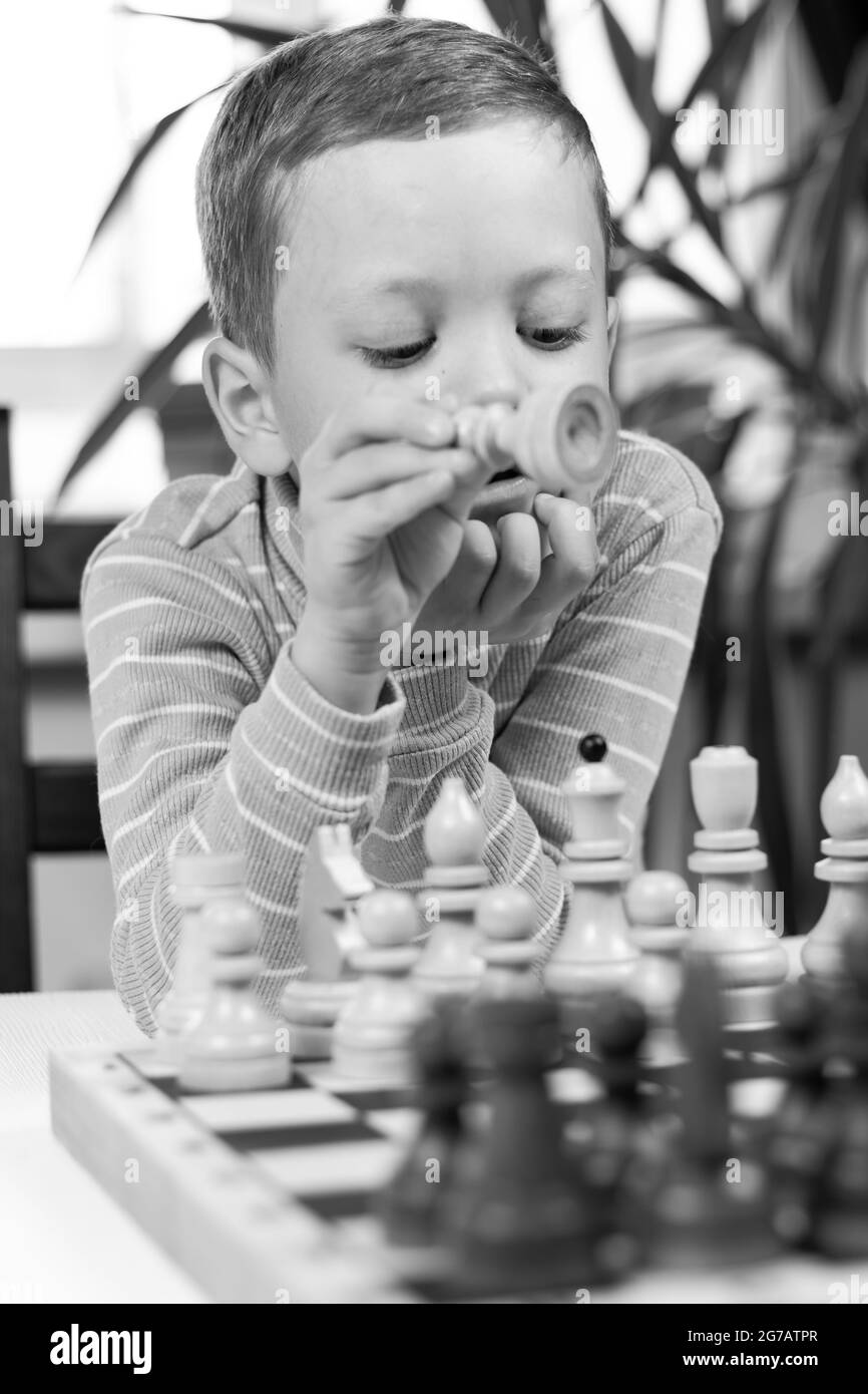 Netter siebenjähriger Junge, der zu Hause auf einem weißen Holztisch Schach spielt. Selektiver Fokus. Nahaufnahme. Hochformat Stockfoto