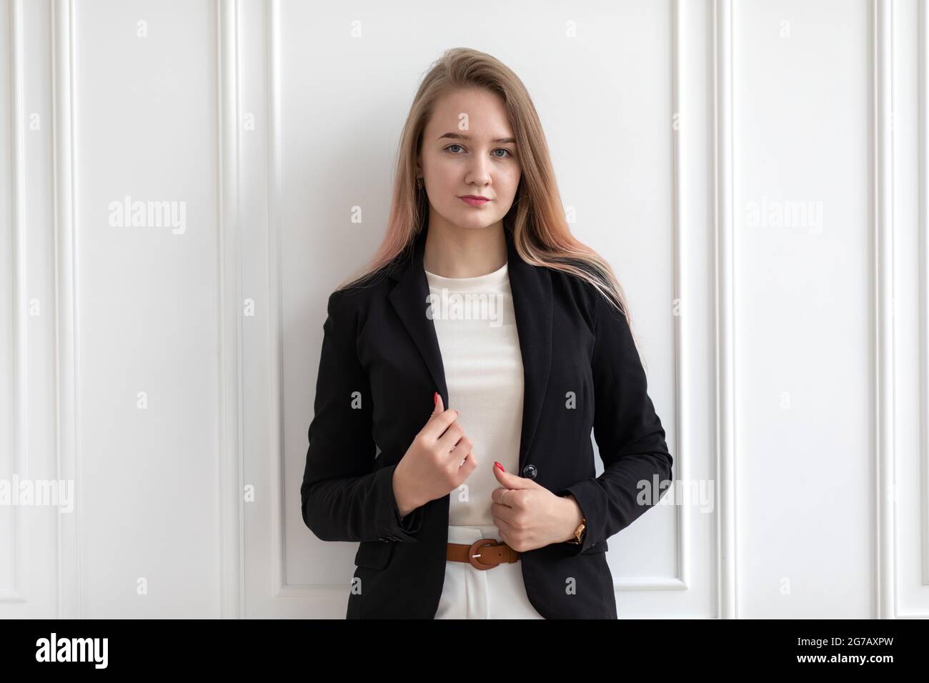 Junge schöne kaukasische Frau in lässiger Bürokleidung stehend und hält schwarze Jacke, posiert, Blick auf die Kamera. Stockfoto