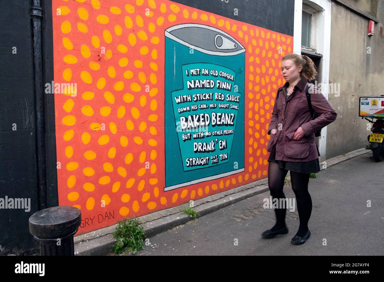 Junge Frau, die an einem Wandbild aus gebackener Beanz-Dose auf der Seite eines Gebäudes in Walthamstow East London vorbeigeht E17 UK England KATHY DEWITT Stockfoto