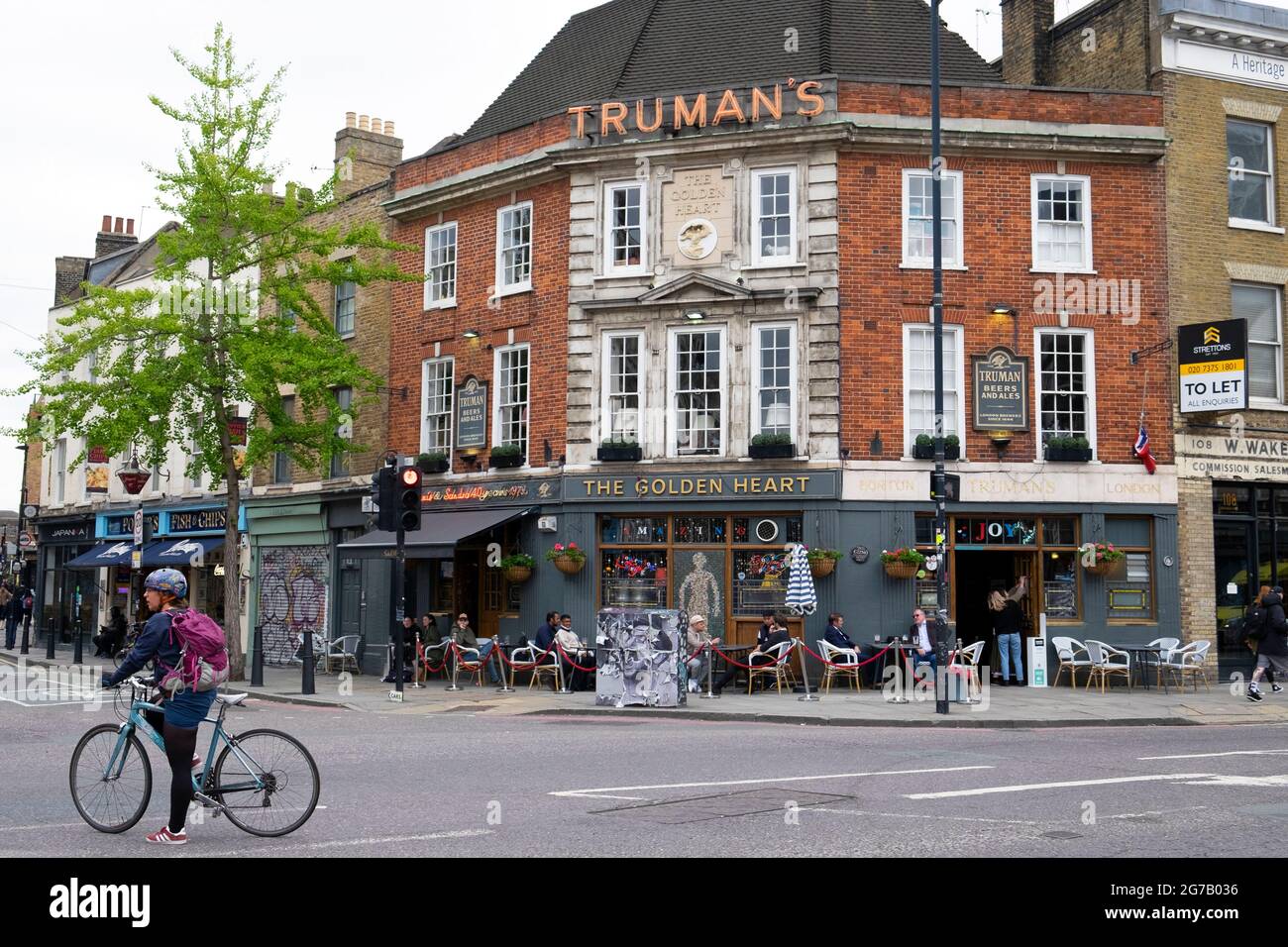 Fahrradfahrer auf dem Fahrrad vor Trumans Pub The Golden Heart an der Ecke Commercial St & Hanbury Street in der Nähe des Spitalfields Market London E1 KATHY DEWITT Stockfoto