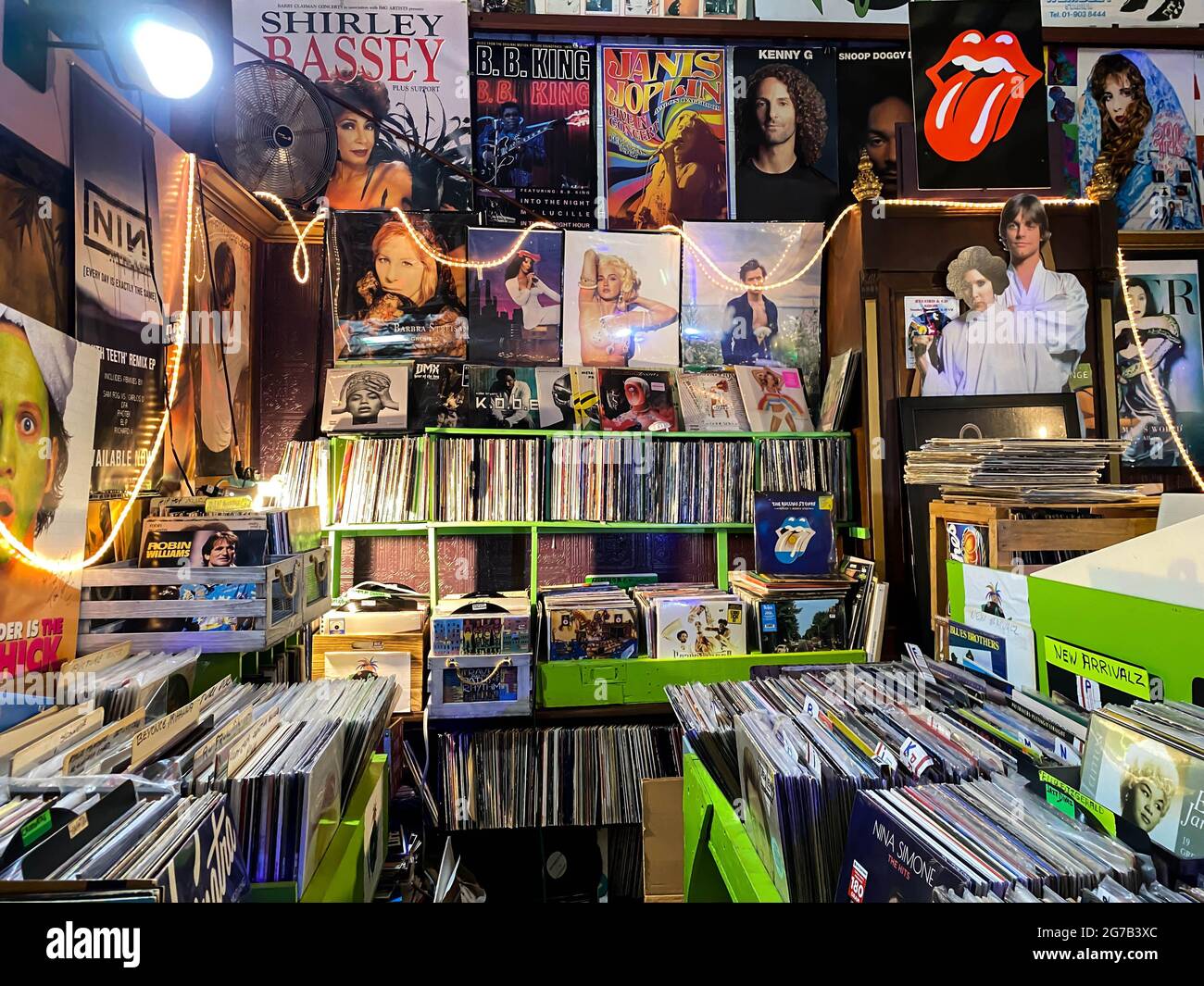 Plattenladen mit Plakaten, die überall an den Wänden verputzt sind, und Vinylplatten-Ständen und -Kisten im gesamten Geschäft zum Verkauf. Stockfoto