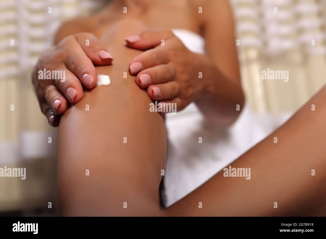 Frau Hände Anwendung Körpercreme auf ihr Bein zu Hause. Das Mädchen trägt ein weißes Handtuch. Konzept für Hautpflege und Schönheit Stockfoto