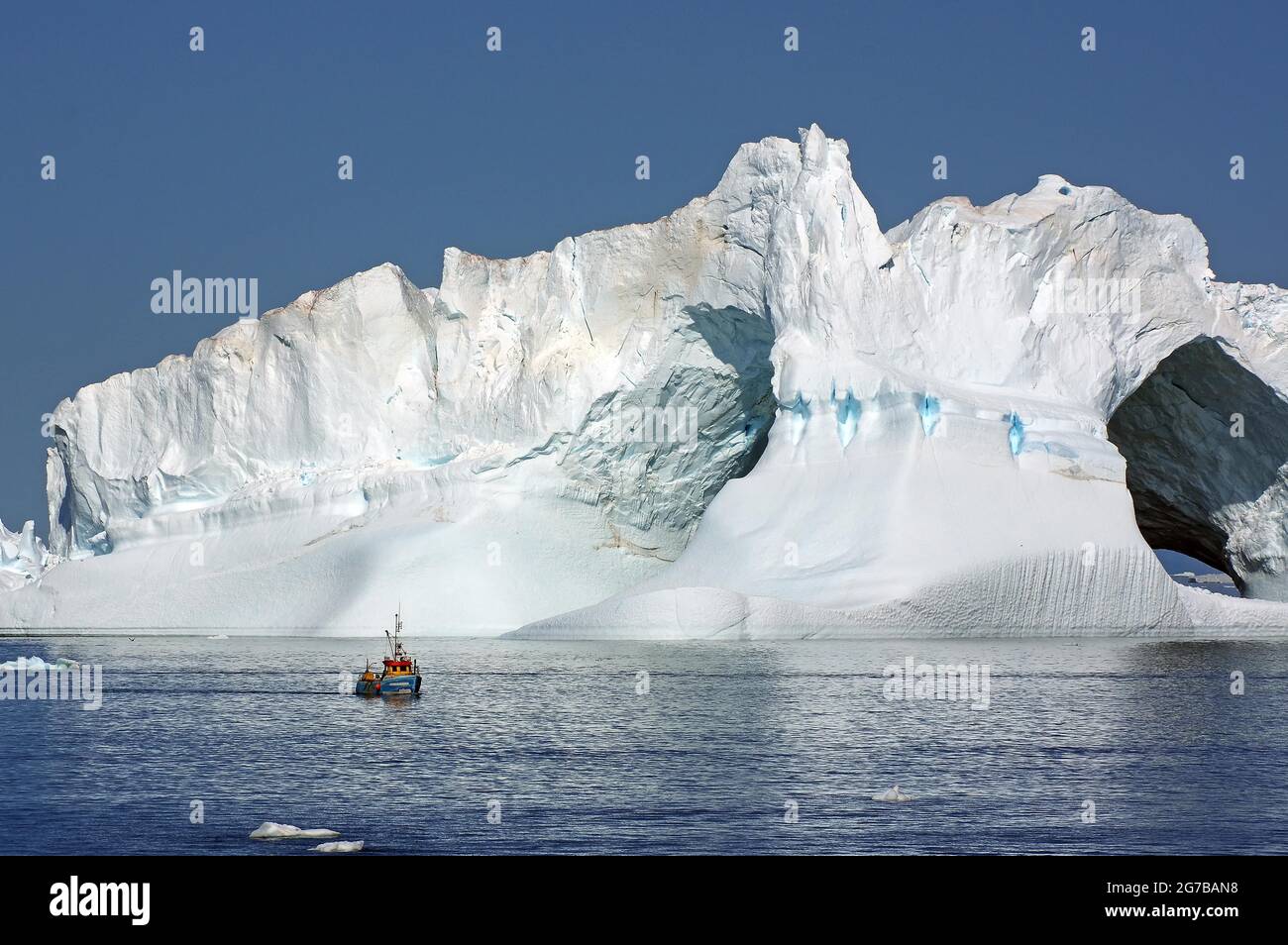 Kleines Fischerboot vor einem riesigen Eisberg mit zwei Löchern, Disko Bay, Ilulissat, Grönland, Dänemark Stockfoto