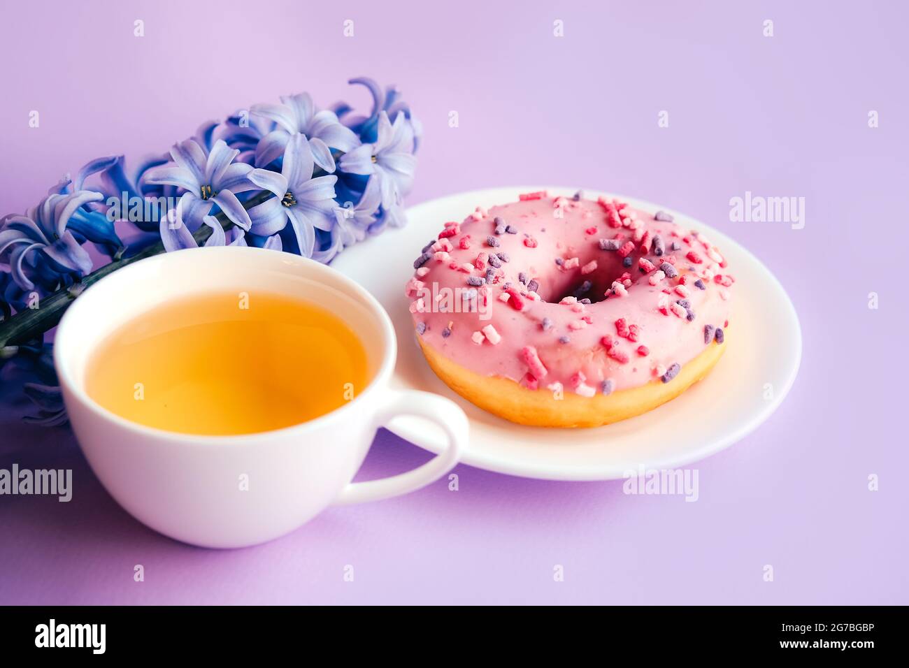 Rosa Zucker glasierte Donut, Tasse Tee und lila Hyazinthe Blume auf buntem Hintergrund. Stockfoto