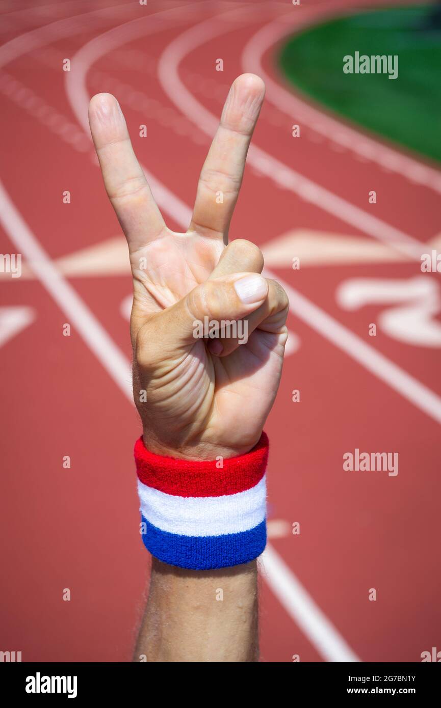 Amerikanischer Athlet mit rot-weißem Schweißband am Handgelenk, das ein V-Zeichen für den Sieg mit der Hand auf einer Laufstrecke macht Stockfoto