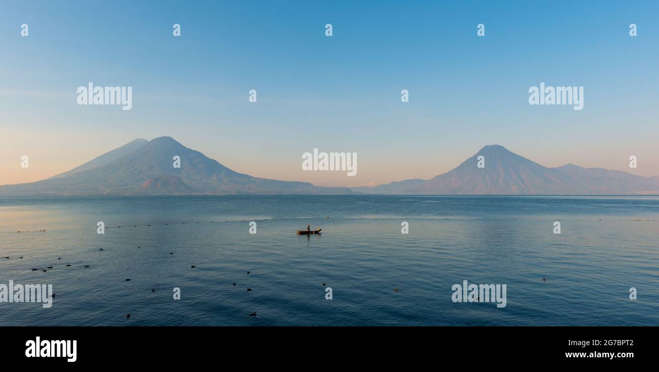 Atitlan Lake Panorama mit maya indigenen Mann in Fischerboot und Vulkan bei Sonnenaufgang, Panajachel, Guatemala. Stockfoto