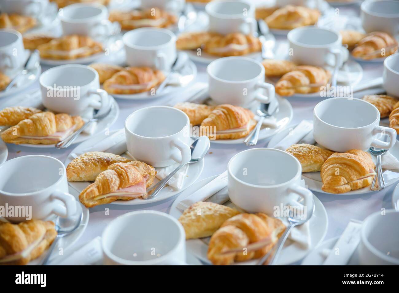 Viele Croissants auf einer Schüssel mit leeren Kaffeetassen auf dem Tisch, die für die Teepause auf einer Geschäftskonferenz serviert werden können Stockfoto