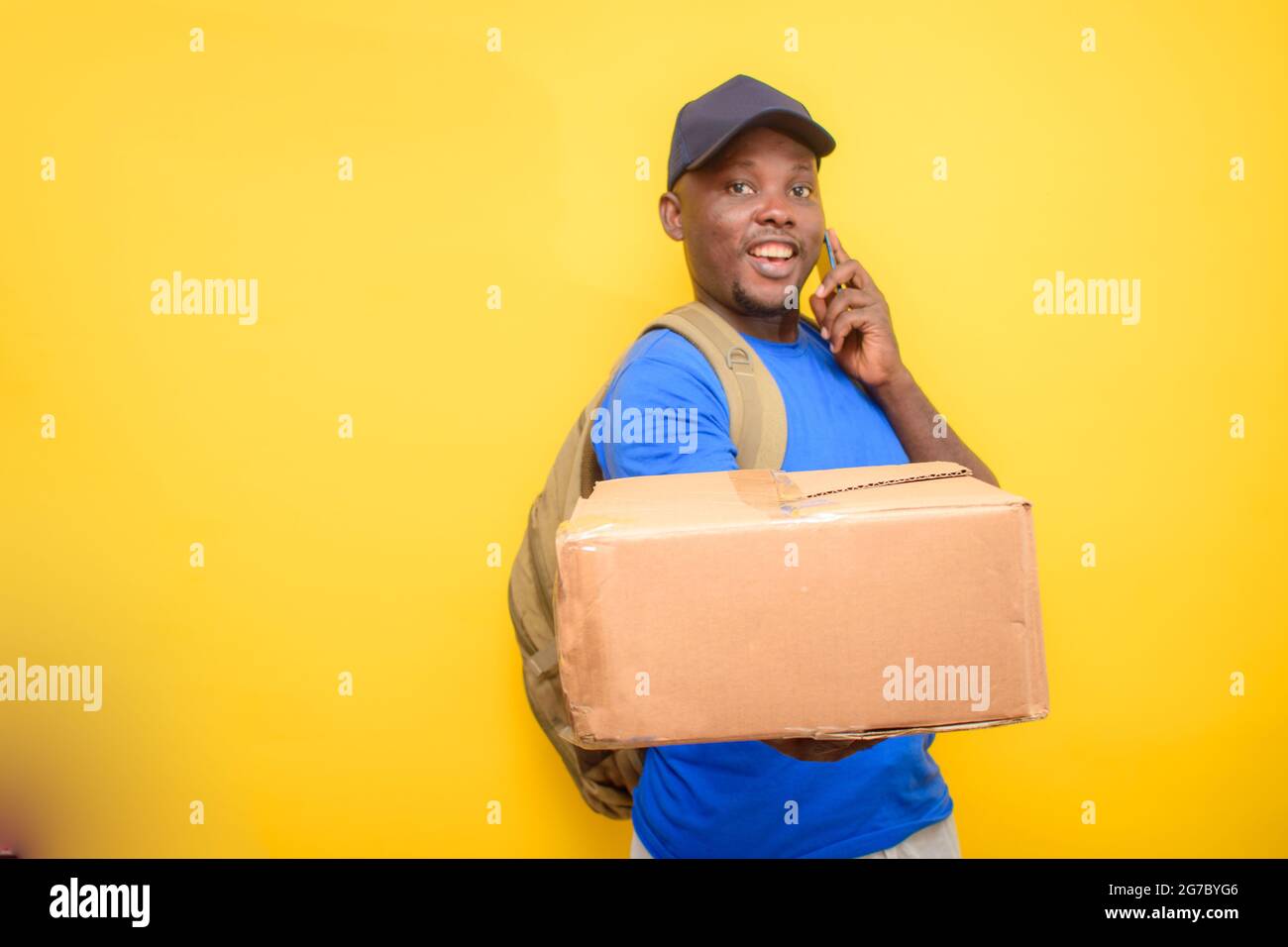Ein afrikanischer Entsendungsmann mit Rucksack, der einen Anruf abgab, Boxen trug und eine Gesichtskappe trug Stockfoto