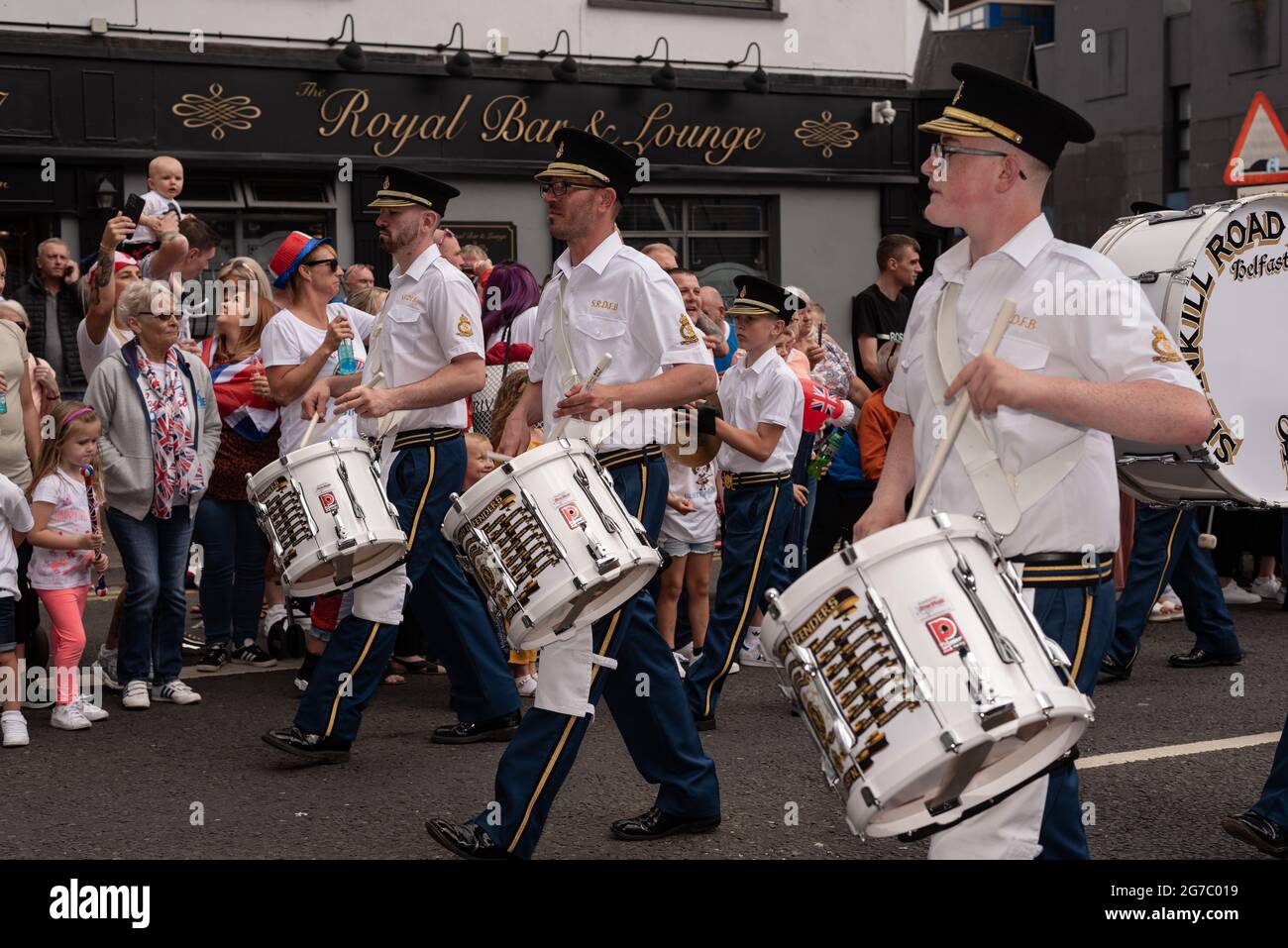 Zuschauer beobachten und jubeln, Mitglieder der Band spielen Trommeln auf der Shankill Road, einem überwiegend loyalistischen Viertel.Jeden Sommer, mit Ausnahme des letzten Jahres aufgrund von Covid-19, marschieren Demonstranten durch die Straßen von Belfast für die Parade vom 12. Juli/Orange March, um die Schlacht von Boyne zu feiern. Orange Walks sind während der gesamten Ordensexistenz sowohl von Katholiken als auch von Nationalisten kritisiert worden, die sie als sektiererisch und triumphierend empfinden. Trotz einer Geschichte öffentlicher Unruhen während der Paraden sowie protestantischer Unzufriedenheit und Frustration aufgrund der jüngsten Brexit-Abkommen, Stockfoto