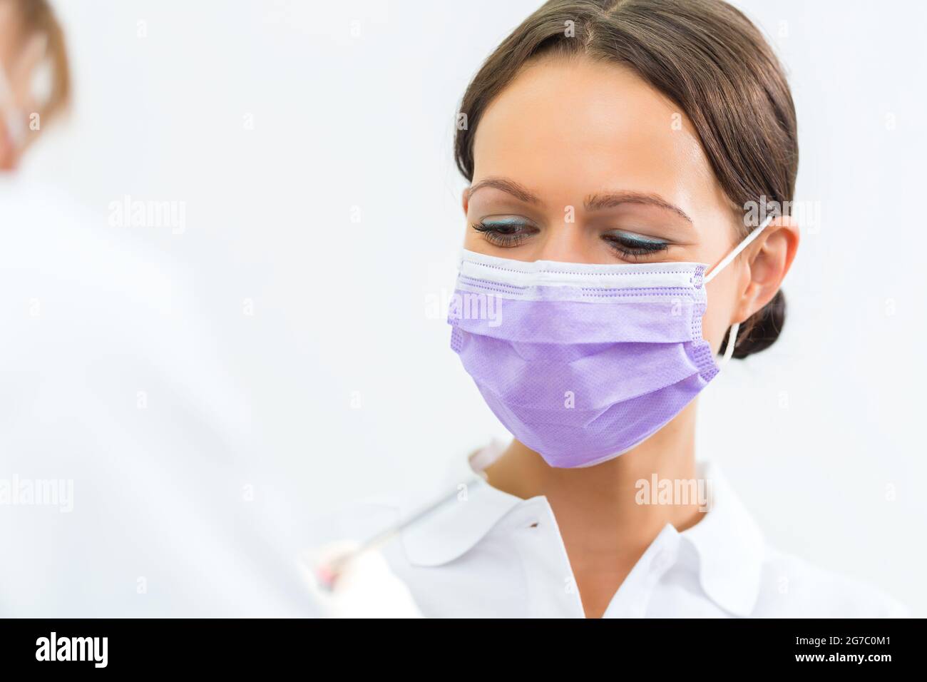 Zahnärztin in ihrer Praxis oder ihrem Büro, die männlichen Patienten mit behandelt Assistent trägt Maske Stockfoto