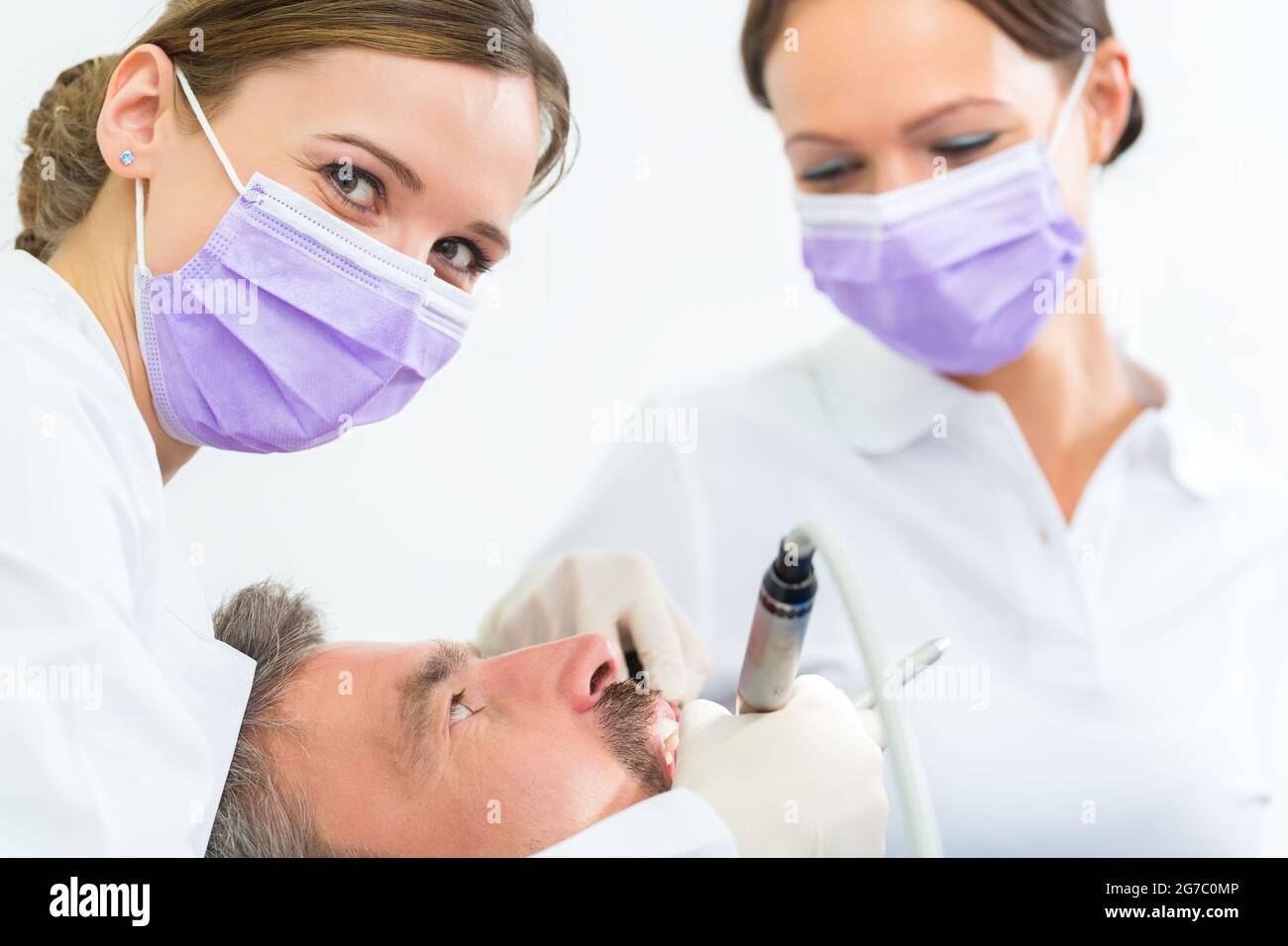 Zahnärztin in ihrer Praxis oder ihrem Büro, die männlichen Patienten mit behandelt Assistent mit Masken und Handschuhen Stockfoto