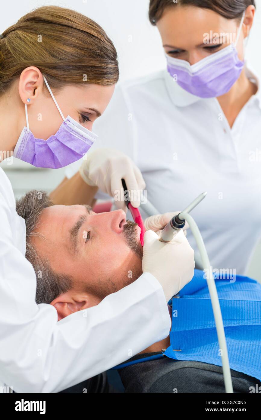 Zahnärztin in ihrer Praxis oder ihrem Büro, die männlichen Patienten mit behandelt Assistent mit Masken und Handschuhen Stockfoto