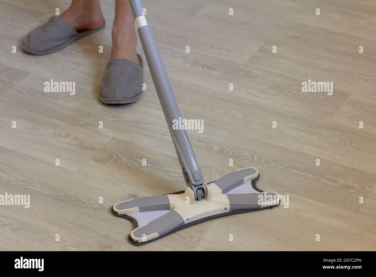 Ein junger Mann in Hausschuhen reinigt den Boden mit einem Mopp. Stockfoto