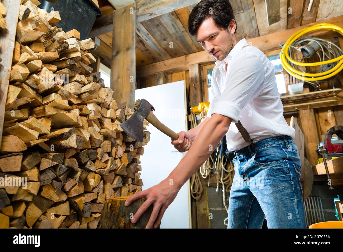 Junger Mann hackt Holz oder Holz mit einem Beil oder Axt in einer Hütte in den Bergen Stockfoto