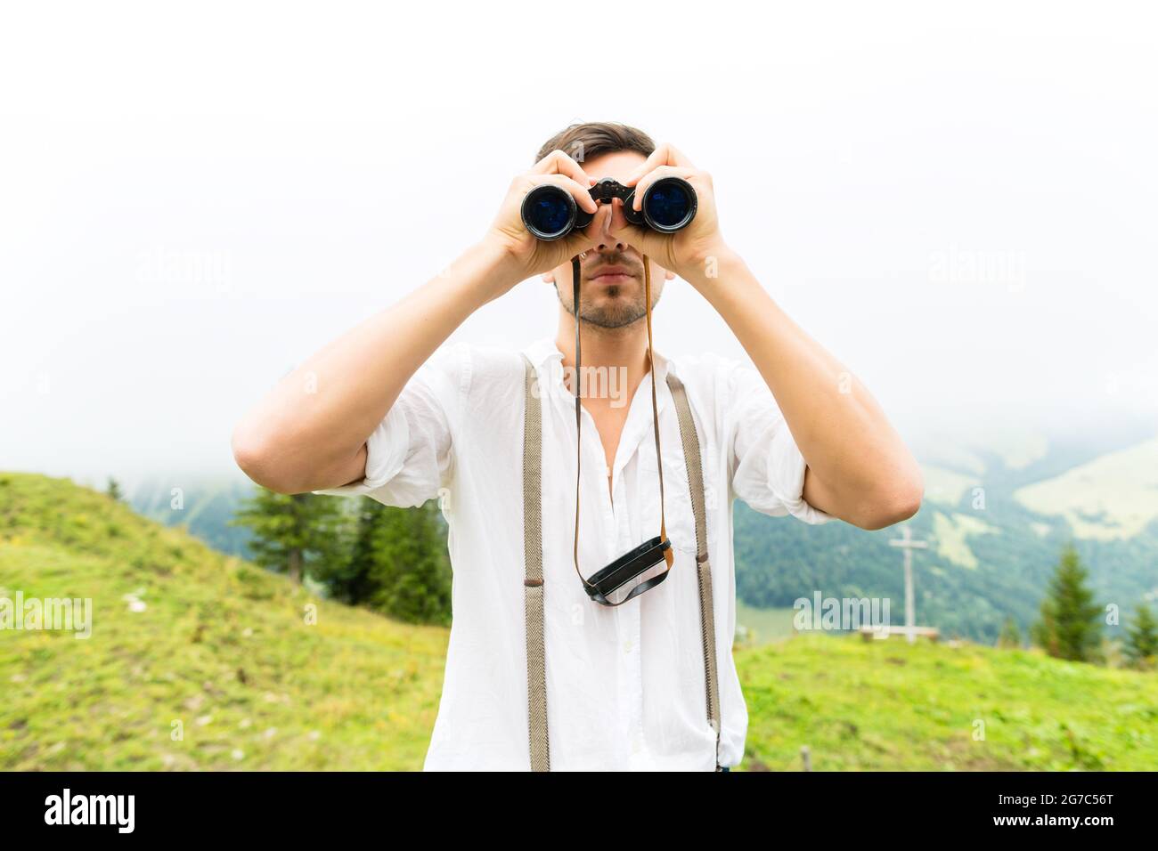 Wandern - junger Mann in den bayerischen Alpen schaut durch Eine Feldbrille oder Fernglas genießen das Panorama in der Freizeit oder Urlaub Stockfoto