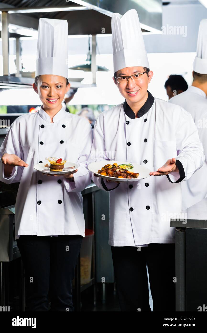 Asiatische indonesischen Koch zusammen mit anderen Köche im Restaurant oder Hotel kommerzielle Küche kochen, schlichten Schale oder Platte Stockfoto