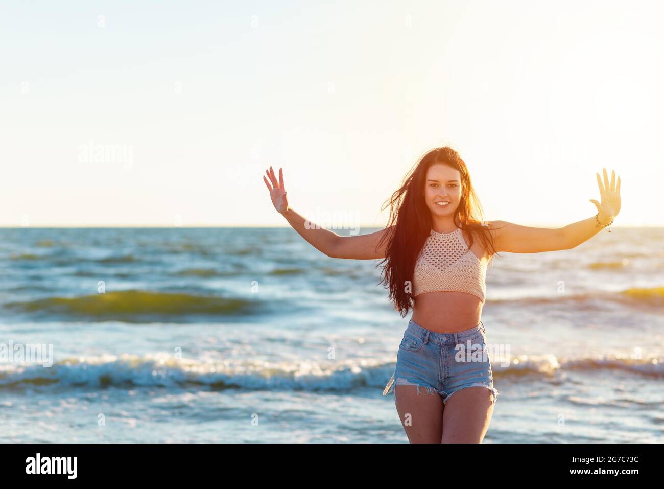 Schöne sexy Mädchen heben die Hände auf dem Meer Strand in einer lässigen Kleidung schaut auf die Kamera bei Sonnenuntergang. Nahaufnahme eines modischen Mädchen.schönes Porträt von Stockfoto