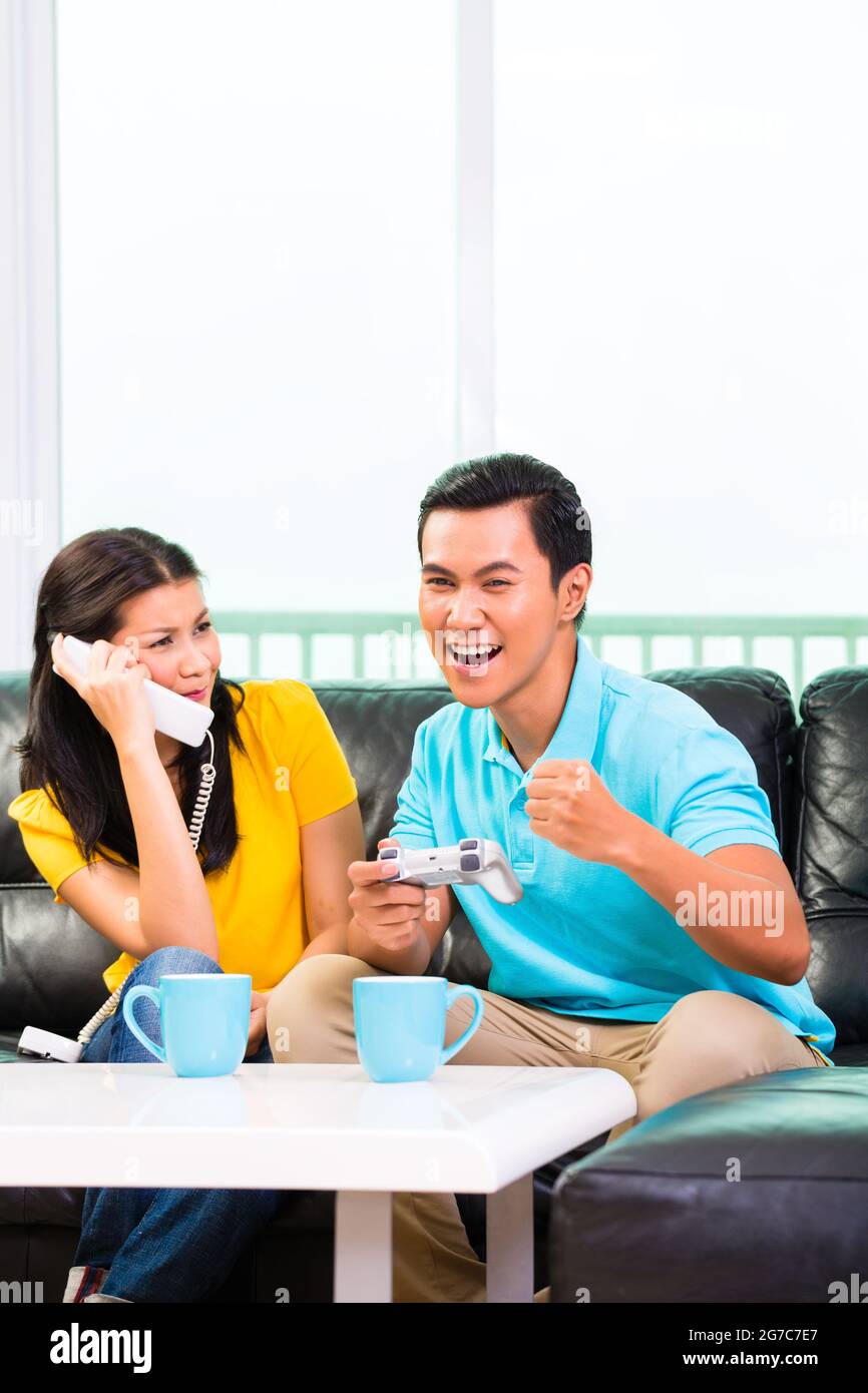 Jungen Asiatischen stattlichen Paare in der Freizeit zusammen und spielen mit laptop Video Game Konsole und Handy auf der Couch Stockfoto