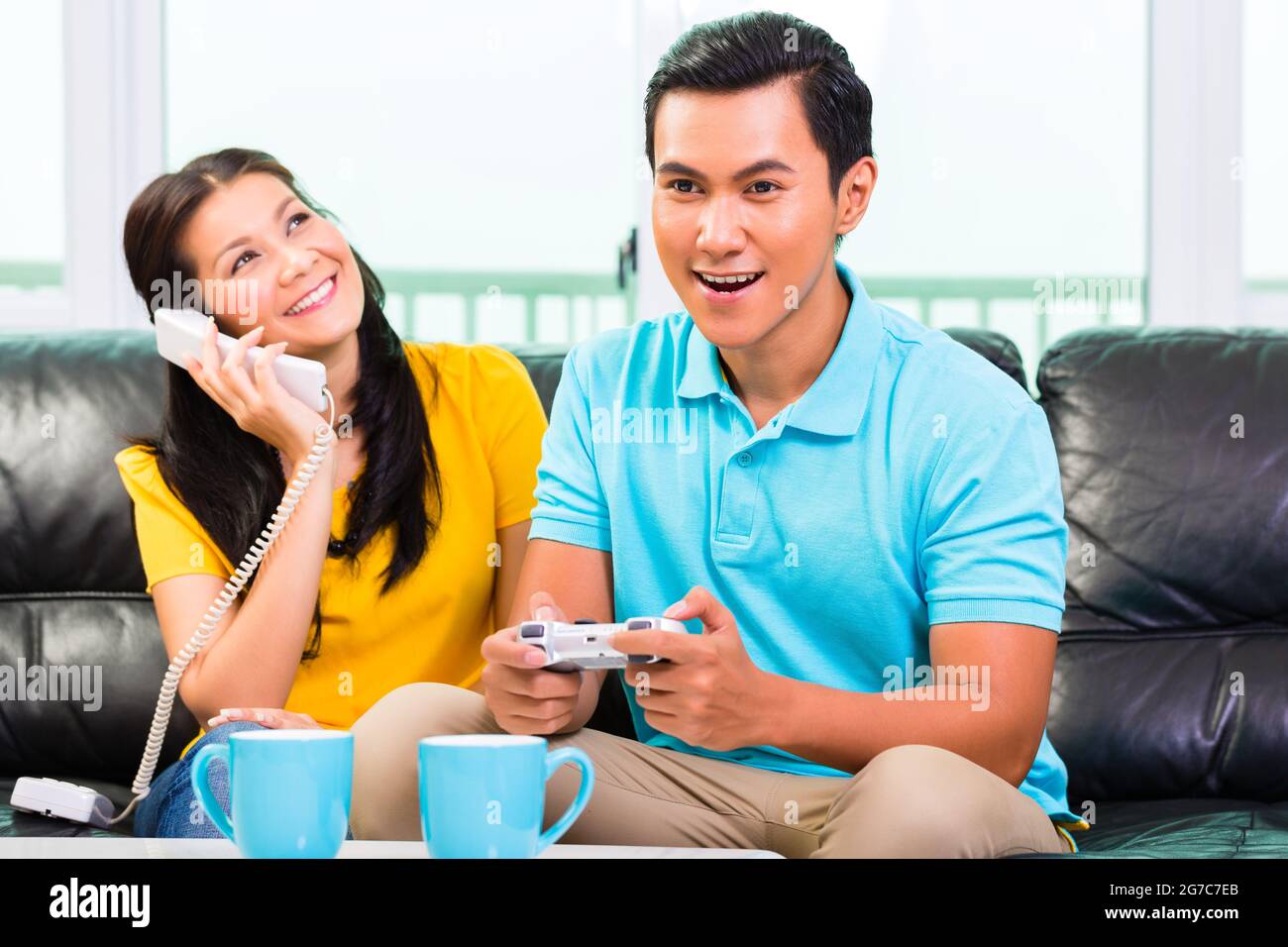Jungen Asiatischen stattlichen Paare in der Freizeit zusammen und spielen mit laptop Video Game Konsole und Handy auf der Couch Stockfoto