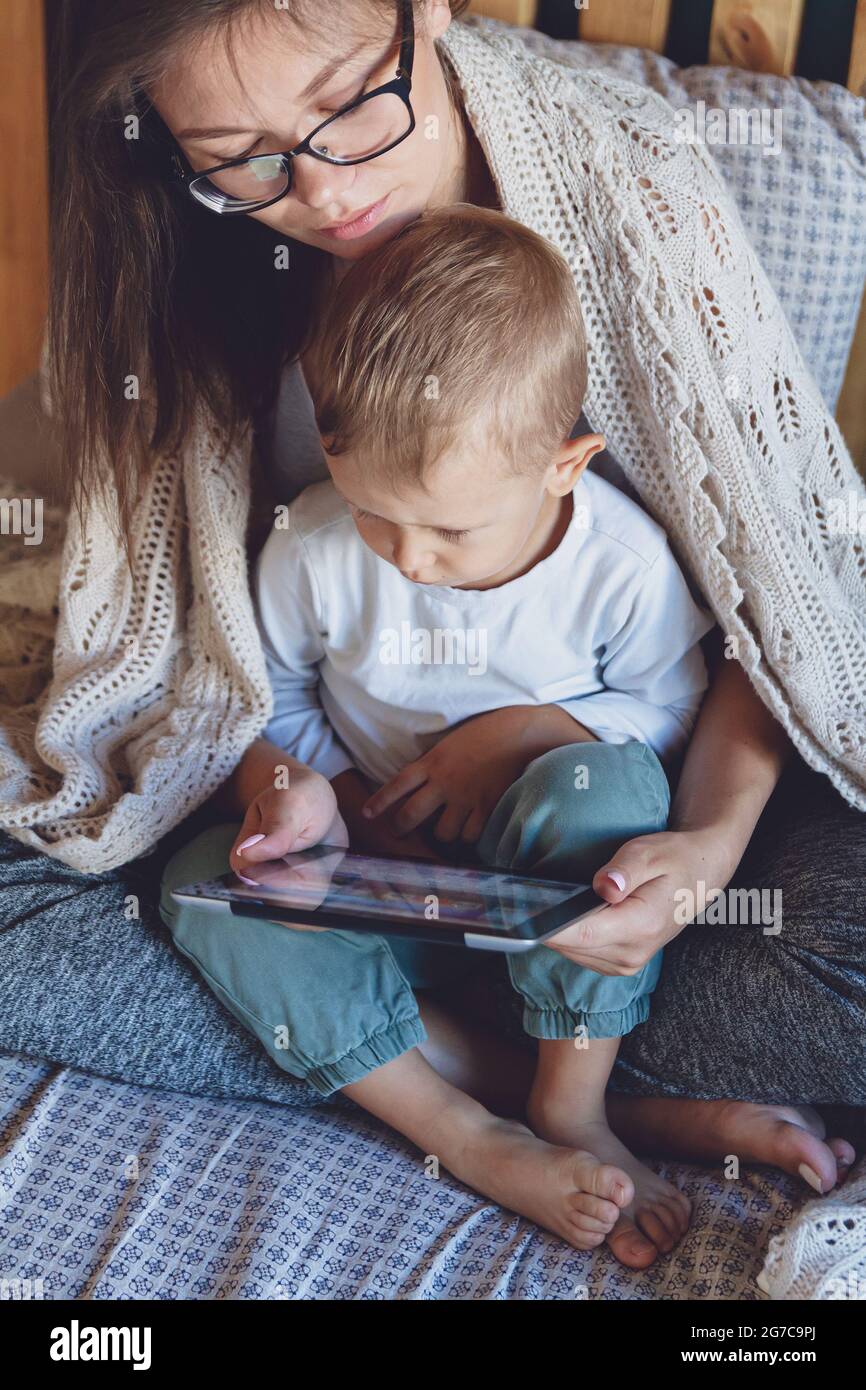 Junge Mutter und Sohn mit einem Tablet unter einer gemütlichen Decke im Bett Stockfoto