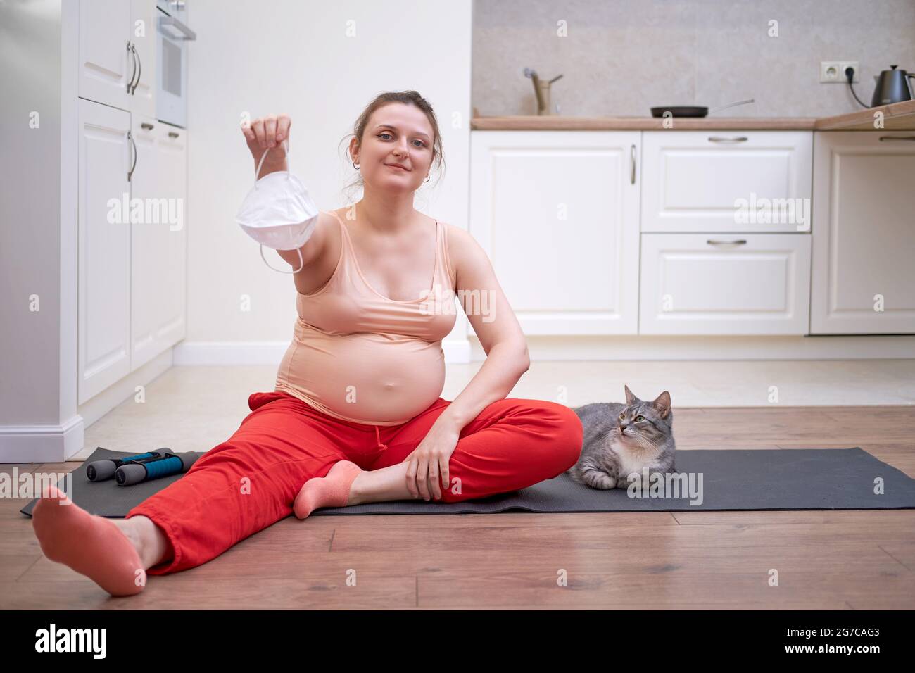 Fitness zu Hause während der Schwangerschaft und die entfernte Gesichtsmaske als Symbol für das Ende der Coronavirus-Epidemie. Schwanger Frau bei einem Sporttraining ses Stockfoto