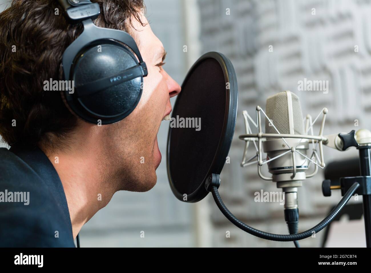 Junge männliche Sänger oder Musiker mit Mikrofon- und Kopfhöreranschluss für Audio-Aufnahme im Studio Stockfoto
