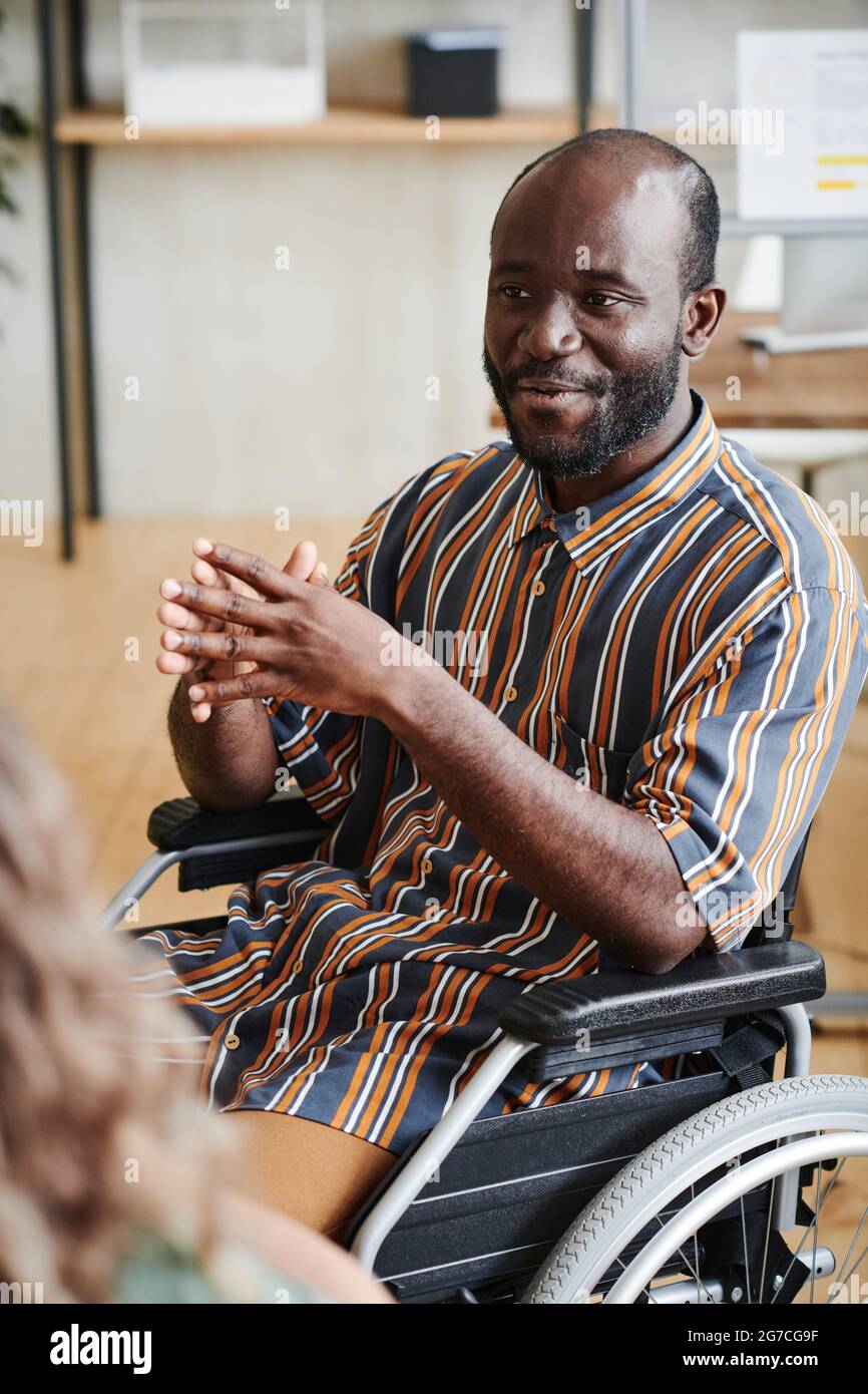 Afrikanischer behinderter Geschäftsmann, der im Rollstuhl sitzt und im Büro mit seinen Kollegen spricht Stockfoto