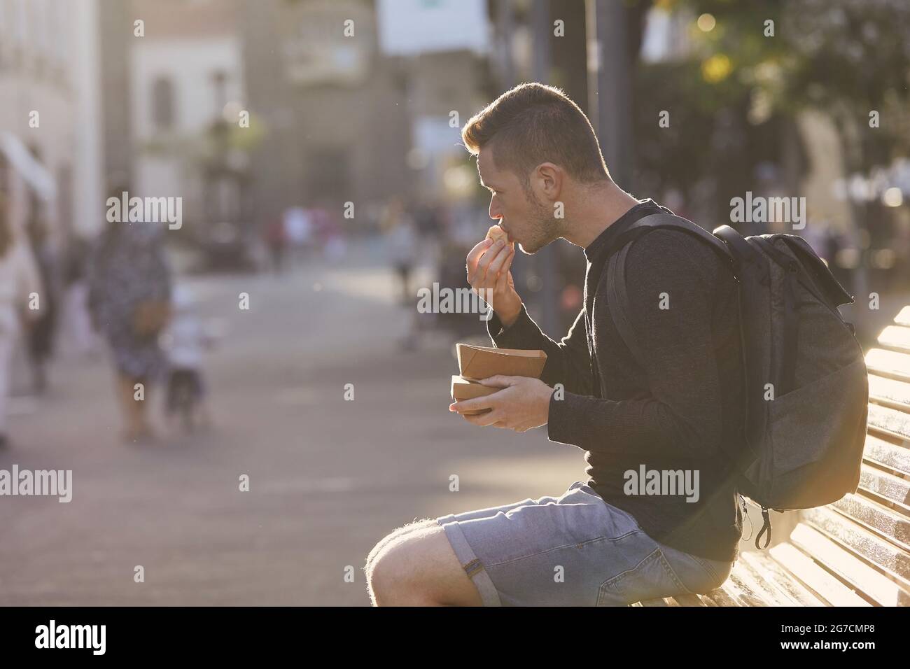 Mann mit Rucksack, der in der historischen Stadt Street Food isst. Tourist in der Altstadt von San Cristobal de La Laguna inTeneriffa, Spanien. Stockfoto