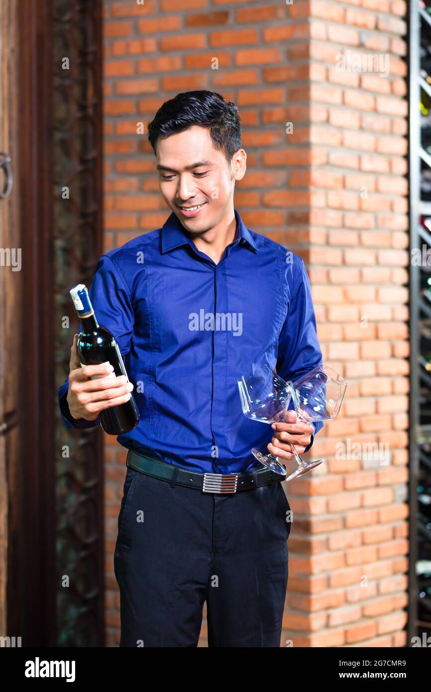 Asiatische Mann hält eine Flasche Wein und Gläser Stockfoto