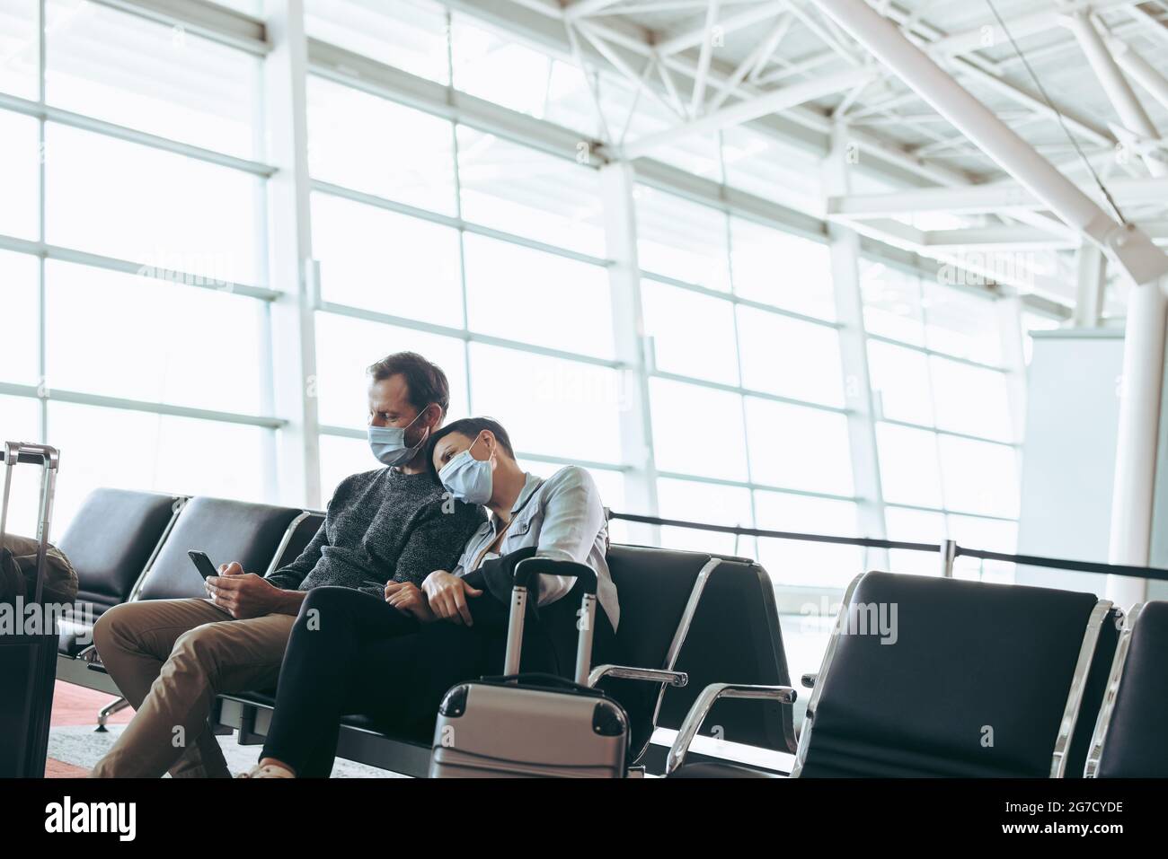 Mann und Frau mit Gesichtsmasken sitzen im Wartebereich des Flughafens. Paar am Flughafen während der Corona-Virus-Sperre. Stockfoto