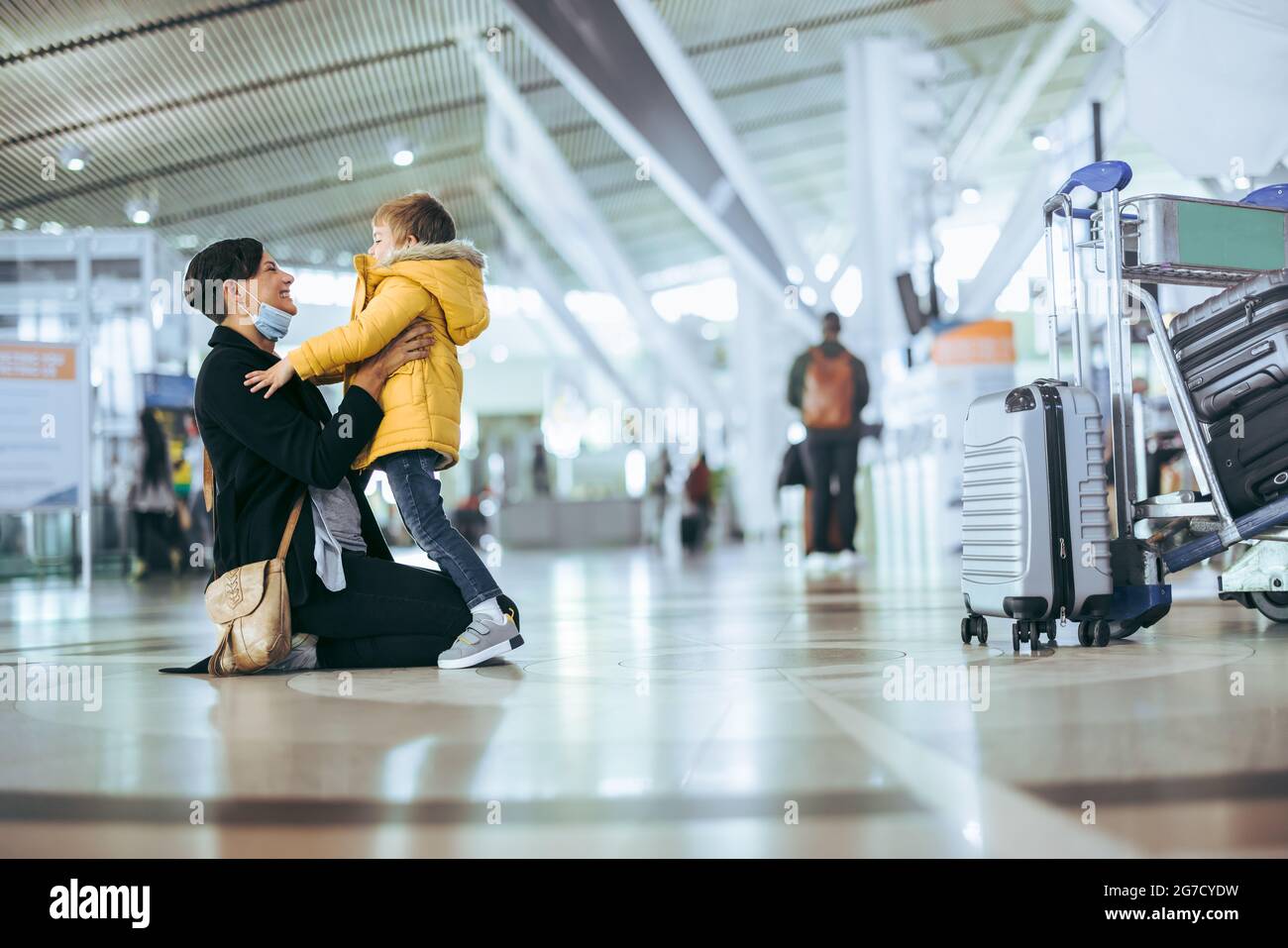 Junge trifft seine Mutter am Flughafen nach langer Trennung während einer Pandemie. Glückliche Frau, die bei der Ankunft am Flughafen den Sohn trifft. Stockfoto