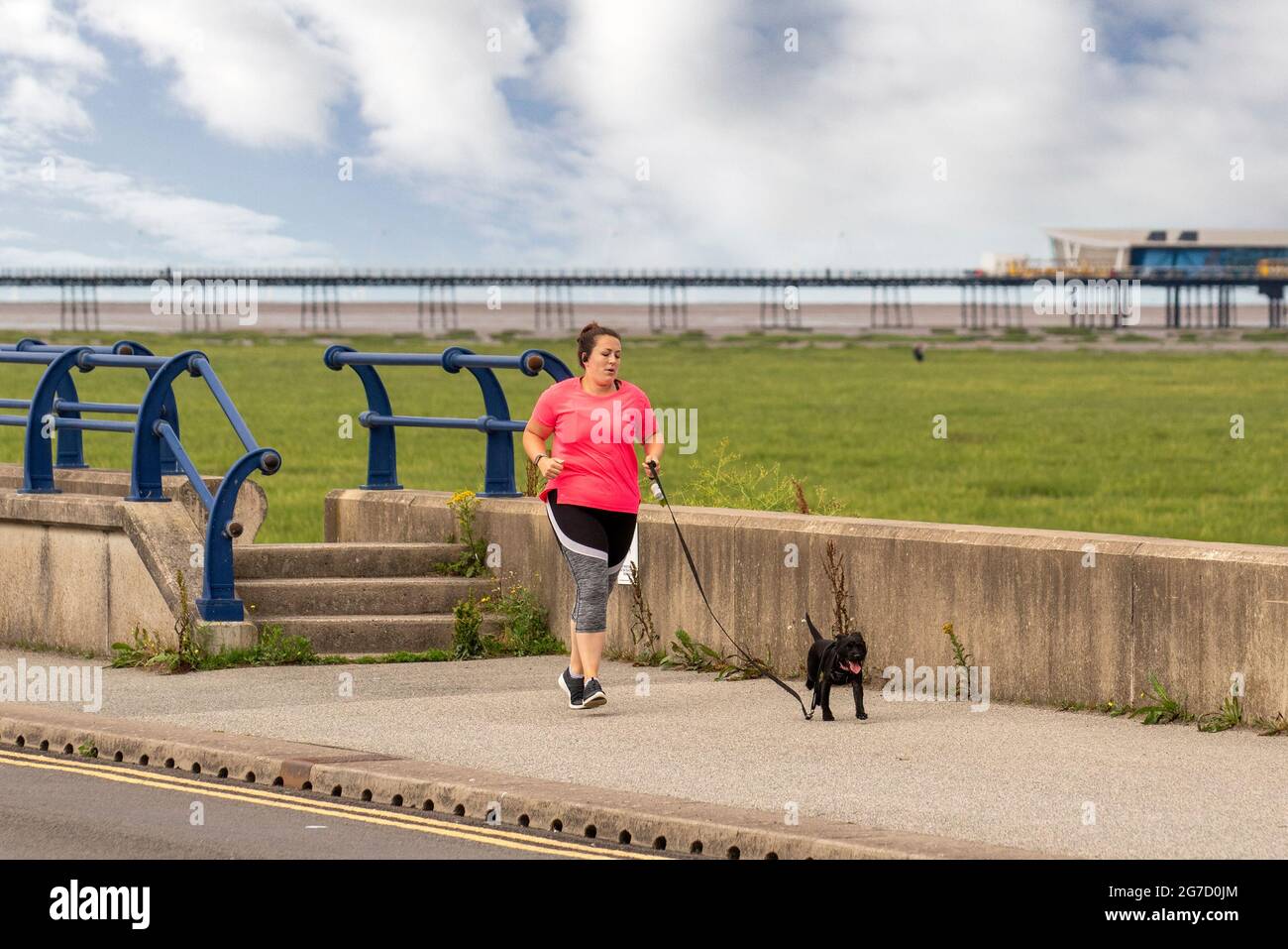 Southport, Merseyside. Wetter In Großbritannien. 13. Juli 2021: Früher Sonnenschein und wärmende Temperaturen erreichen 20 Grad, während die Anwohner an der Strandpromenade des Resorts leichte Übungen machen. Aktivitäten auf der Küstenstraße als Lebensraum für Dünen und die Vergrabung des Sandes (Akkretion) scheinen sich bis zur Fylde-Küste auszudehnen. Die Sefton-Küste kämpft darum, zwei Eindringlinge abzuwehren – das Meer und zähe Gräser, die über dem Strand sprießen und schließlich den Pier umringen, wenn sich Sanddünen bilden. Kredit; MediaWorldImages/AlamyLiveNews Stockfoto