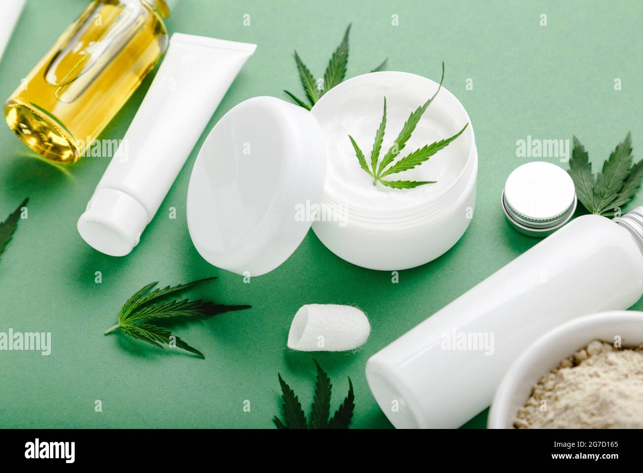 Hanf feuchtigkeitsspendende Creme im weißen Glas mit CBD-Öl Cannabis Blatt und Set Hautpflege Kosmetik auf grünem Hintergrund Stockfoto