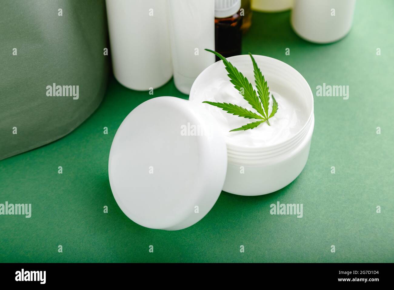 Hanf feuchtigkeitsspendende Creme im weißen Glas mit CBD-Öl Cannabis Blatt und Set Hautpflege Kosmetik auf grünem Hintergrund Stockfoto