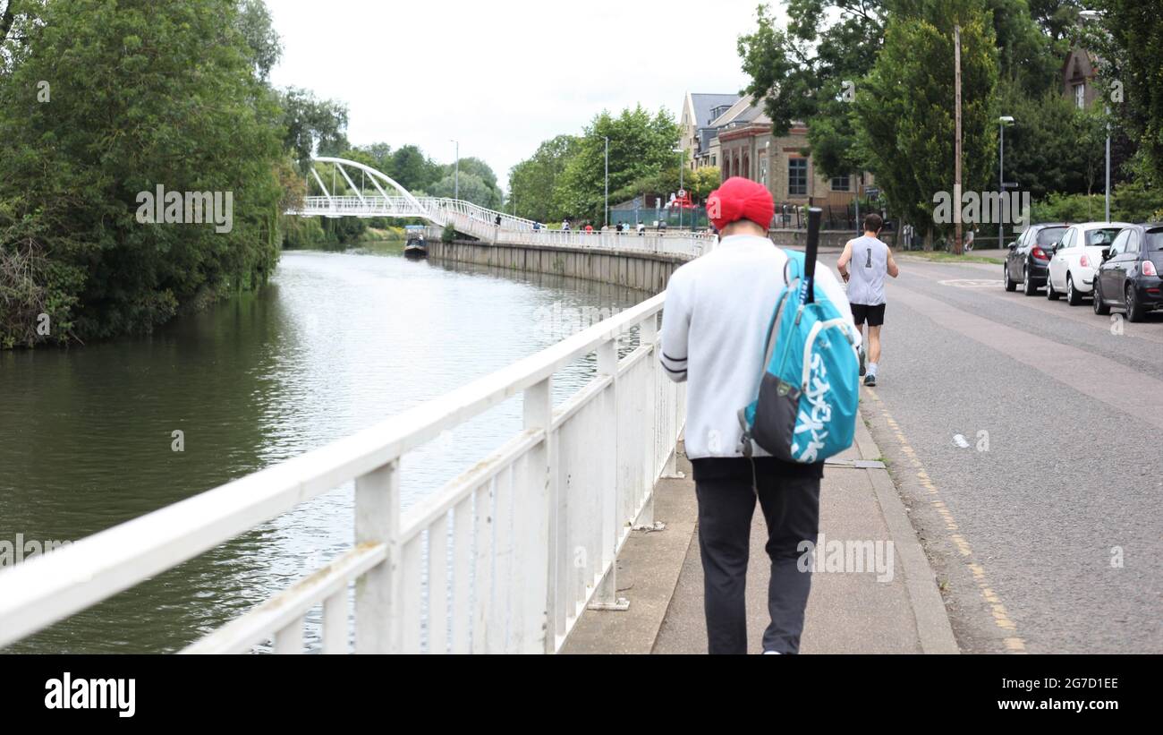 Sport & Freizeit Lifestyle-Konzept - Rückansicht eines jungen Sikh-Mannes mit Badminton-/Tennisschläger in seiner Jacke entlang des Flusses Cam in Cambridge, Großbritannien Stockfoto