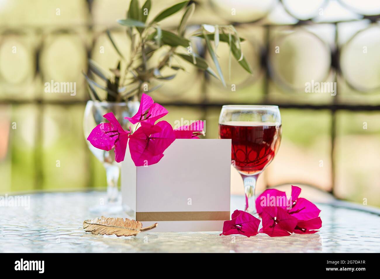 Elegantes Glas Rotwein. Dekorative rosa Blüten von Bougainvillea. Nachbau einer Postkarte oder Einladung. Festliches Weihnachtskonzept. Dekorative grüne Leine Stockfoto