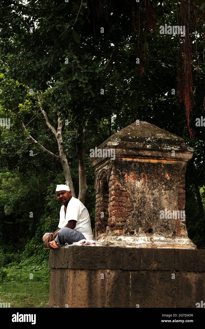 11. Juli 2021 im Dorf Mardhe, Satara, Indien. Indischer, nicht identifizierter alter Mann, der morgens vor dem kleinen Tempel sitzt, ländlicher Lebensstil. Indian Village Stockfoto