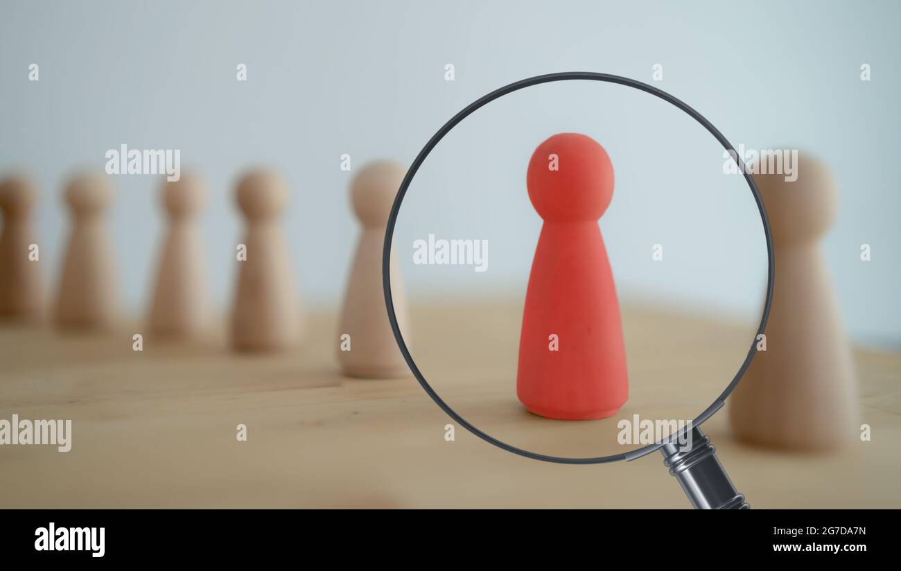 Der Blick durch die Lupe auf die eine hölzerne rote Person zwischen anderen Menschen. Ressourcenmanagement, Rekrutierung, Einstellung, Headhunting-Konzept. Finde le Stockfoto