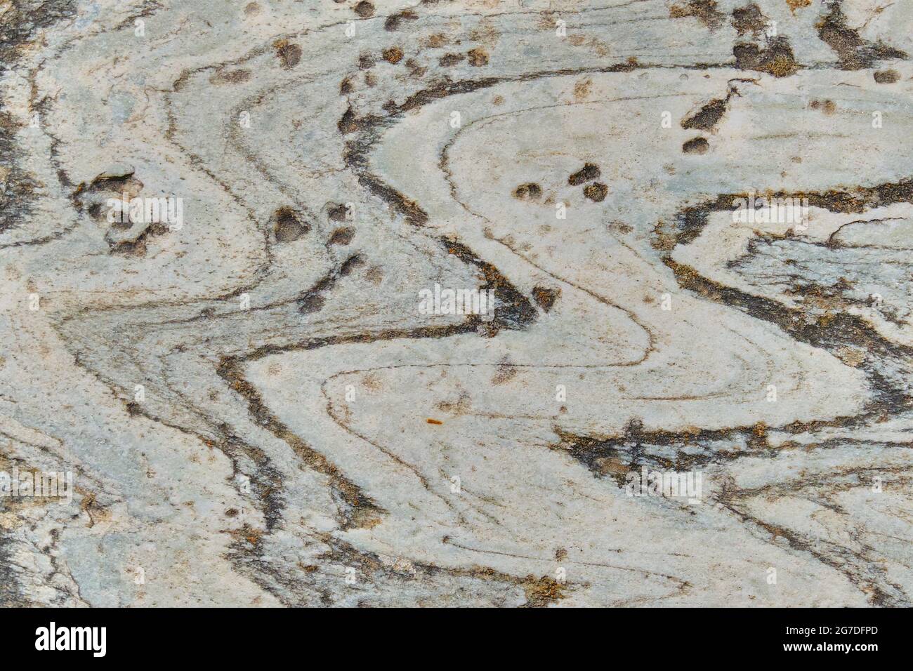 Hintergrund grauer Stein mit Flecken von Rost. Natürliches Gestein von unheilvoller Herkunft mit Eisen. Struktur aus grauem Stein mit Wellenmuster. Stockfoto