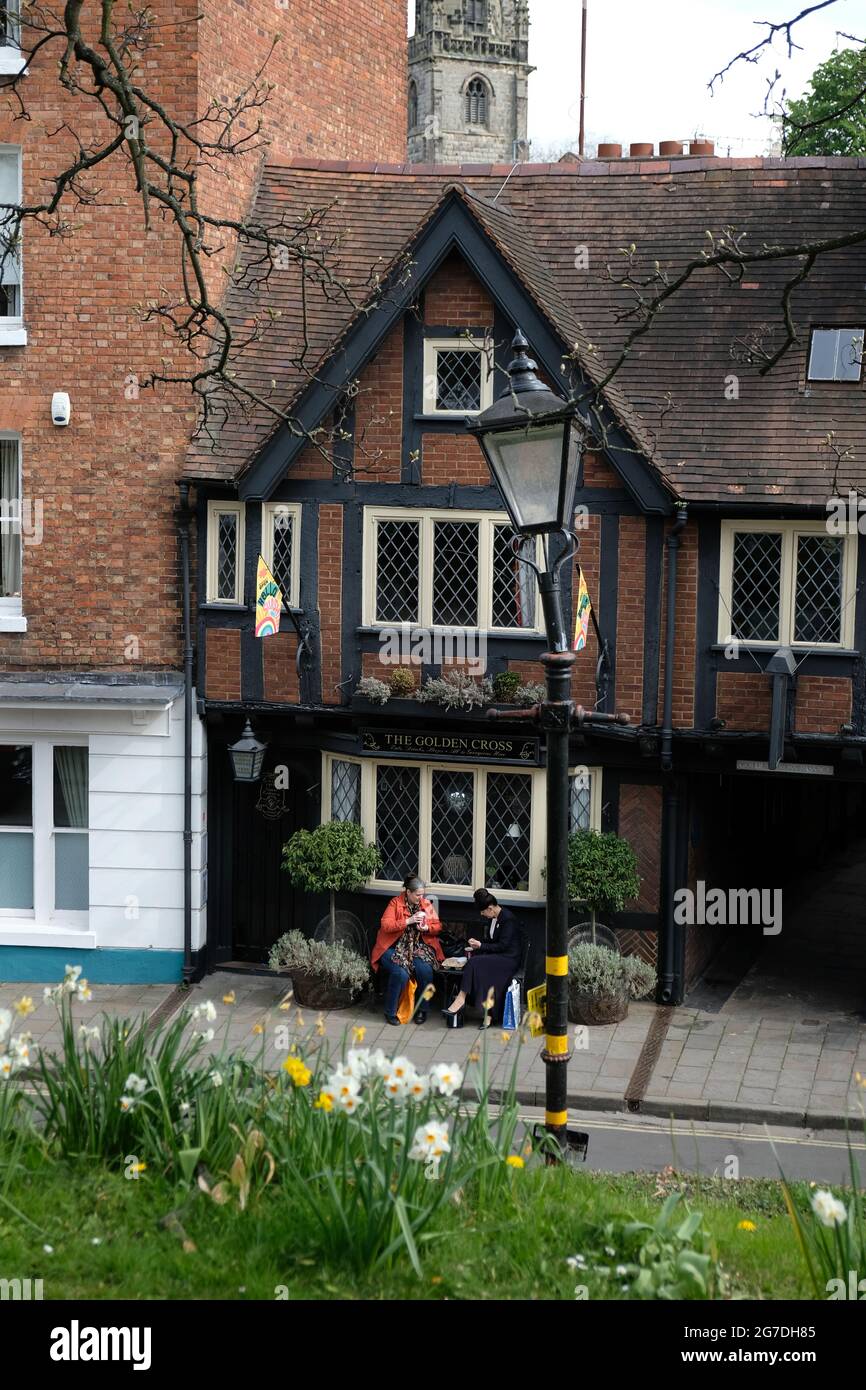 Zwei Frauen sitzen draußen in der Princess Street, Shrewsbury, Shopshire. Sie trinken Kaffee und Snacks. Narzissen im Vordergrund St. Alkmund's im Hintergrund Stockfoto