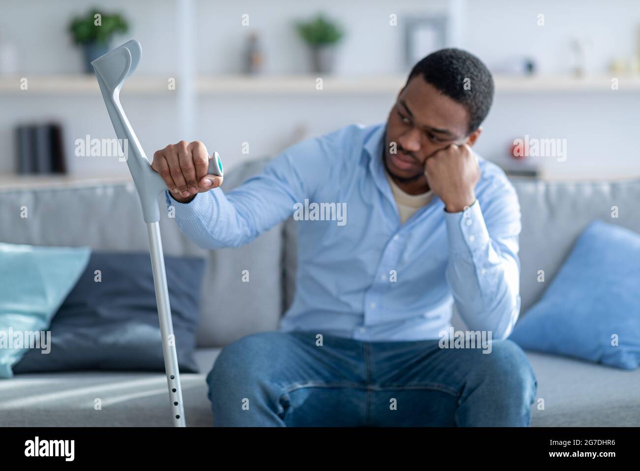 Unglücklicher afroamerikanischer Kerl, der sich an Krücke lehnt, an Depressionen nach Verletzungen zu Hause leidet, selektiver Fokus Stockfoto